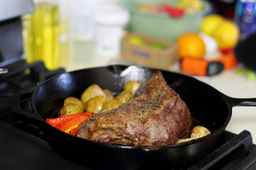 Sirloin tritip steak in a cast iron pan with potatoes and onions on the stove top.