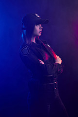 Serious female police officer is posing for the camera against a black background with red and blue backlighting.