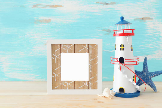 Nautical concept with empty photo frame and lighthouse over wooden table. For photography montage
