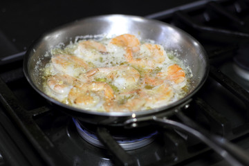 Shrimp scampi cooking in butter and garlic in a stainless steel skillet on the stove.