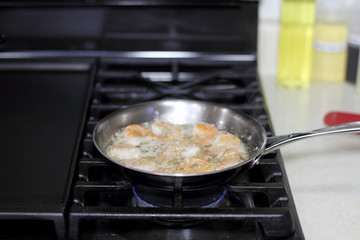 Shrimp scampi cooking in butter and garlic in a stainless steel skillet on the stove.