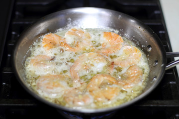 Shrimp scampi cooking in butter and garlic in a stainless steel skillet on the stove.