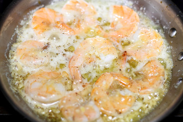 Shrimp scampi cooking in butter and garlic in a stainless steel skillet on the stove.