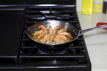Shrimp scampi cooking in butter and garlic in a stainless steel skillet on the stove.