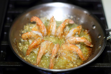 Shrimp scampi cooking in butter and garlic in a stainless steel skillet on the stove.