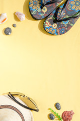 Vacation and summer holidays concept. Flat lay of straw hat, sunglasses, flip flops and seashells on yellow background
