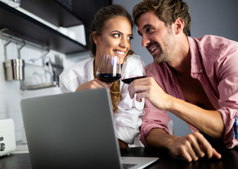 Young couple relaxing in kitchen with wine and laptop. Love, technology, people concept.