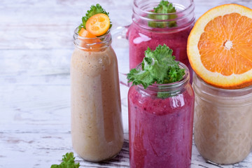 Berry and fruit smoothies in glass jars topped with mint and kumquat slices against the white wooden background