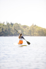 Back view of  attractive young woman siting on paddleboard on quiet sea