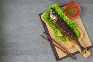 Grilled Saba Fish in wooden dish with seafood sauce on table.
