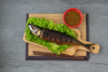 Grilled Saba Fish in wooden dish with seafood sauce on table.
