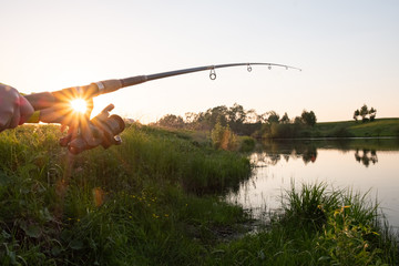 Fishing rod on the lake bent under the weight of fish at sunset. Fishing Rod Sunset Rays