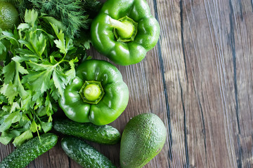Set of green vegetables and fresh greens on a wooden table. Concept of vegetarianism and healthy eating. Top view.