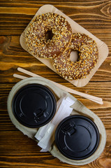 Paper cup for coffee, disposable ecological coffee supplies. Donuts on paper trays. Wooden table.Top view.