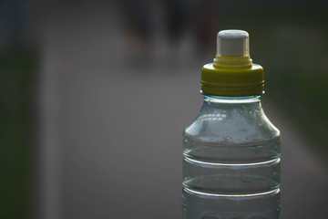 Plastic bottle top full with water with yellow cap in a park or garden with green trees in blurred...