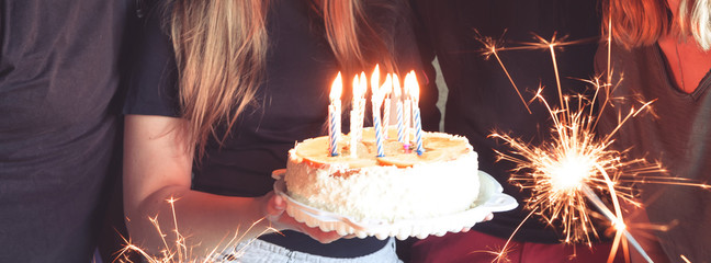 Teen girl blows out candles on a birthday cake with friends and family