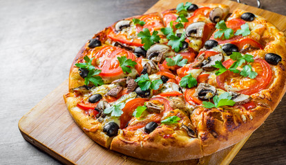 sliced Pizza with Mozzarella cheese, Tomatoes, pepper, olive, mushrooms, Spices and Fresh leaf. Italian pizza on wooden table background