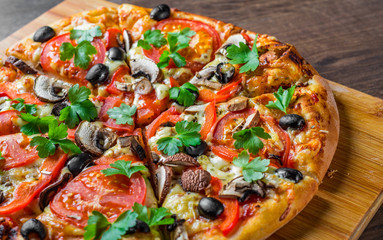 sliced Pizza with Mozzarella cheese, Tomatoes, pepper, olive, mushrooms, Spices and Fresh leaf. Italian pizza on wooden table background