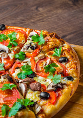 sliced Pizza with Mozzarella cheese, Tomatoes, pepper, olive, mushrooms, Spices and Fresh leaf. Italian pizza on wooden table background