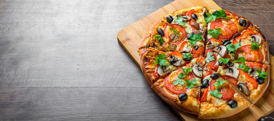 geschnittene Pizza mit Mozzarella-Käse, Tomaten, Paprika, Oliven, Pilzen, Gewürzen und frischem Blatt. Italienische Pizza auf Holztischhintergrund