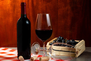 Bottle of red wine in wine cellar for tasting. Red wooden background with wooden box with grapes....