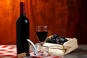 Bottle of red wine in wine cellar for tasting. Red wooden background with wooden box with grapes....