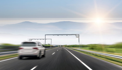 White car drives fast on the highway against the backdrop of a mountain range.