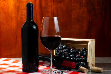 Bottle of red wine in wine cellar for tasting. Red wooden background with wooden box with grapes....