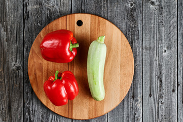 Fresh zucchini and two red Bulgarian peppers on the background of the old board. View from above. Round cutting board with vegetables.