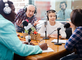 Multinational group of cheerful young adults emotionally discussing in radio studio