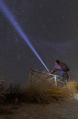 Man with a flashlight looking at the blue night sky with stars and galaxies