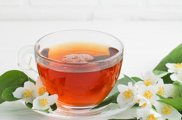 The tea in a glass cup and sprigs of jasmine on a white table. 