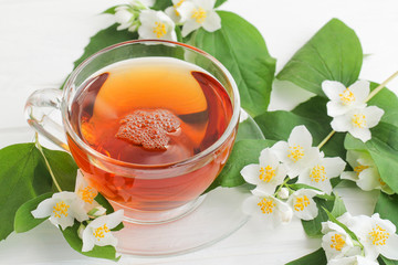 The tea in a glass cup and sprigs of jasmine on a white table. 