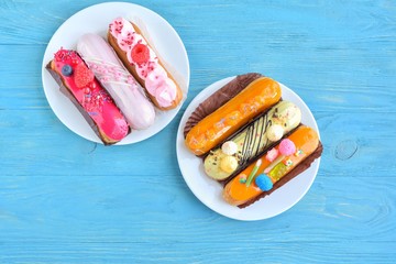 Set of delicious eclairs with creative colorful decor on white plates on the blue textured table....