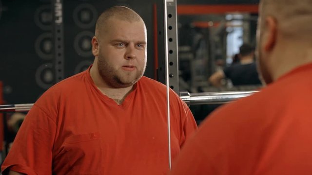 Overweight man holding barbell in hands and workout in gym