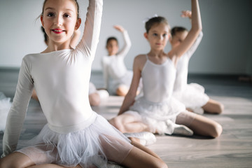 Group of fit happy children exercising ballet in studio together - obrazy, fototapety, plakaty