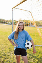 Naklejka premium Portrait of smiling player with soccer ball standing on grassy field against clear sky