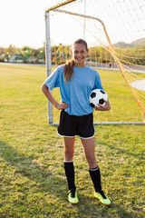 Portrait of smiling player holding ball while standing on soccer field against clear sky © Cavan for Adobe