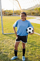 Portrait of soccer player with hand on hip holding ball while standing against net © Cavan for Adobe