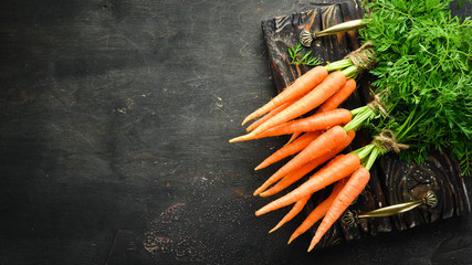 Fresh carrots on a black wooden background. Top view. - obrazy, fototapety, plakaty