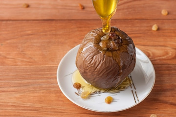 Baked apple stuffed with raisins and walnuts and honey poured on a white plate on a wooden background.