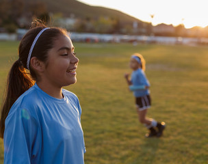 Smiling girl looking away while standing on soccer field against clear sky during sunset © Cavan for Adobe