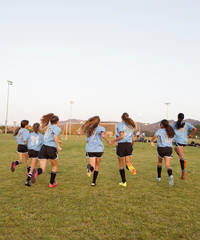 Fototapeta premium Rear view of girls running on soccer field against clear sky during sunset