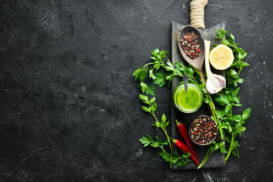 Ingredients for chimichurri sauce: fresh parsley, onion, garlic, olive oil, lemon. On a black background. Top view. free space for your text.