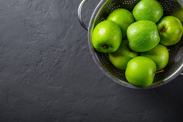 Fresh juicy green apple in stainless steel colander on Dark grey black slate background
