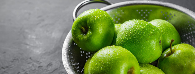 Fresh juicy green apple in stainless steel colander on Dark grey black slate background