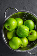 Fresh juicy green apple in stainless steel colander on Dark grey black slate background