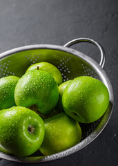Fresh juicy green apple in stainless steel colander on Dark grey black slate background
