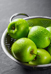 Fresh juicy green apple in stainless steel colander on Dark grey black slate background