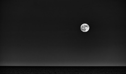 Black and whitr picture of a large moon over the sea in the Natural park in Corralejo Fuerteventura Spain